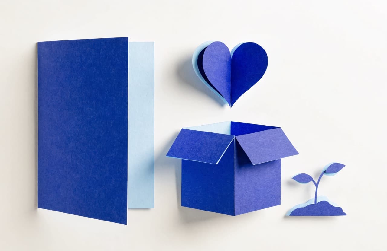 Paper-craft illustration of a letterhead page beside a paper donation box, heart, and sprouting plant